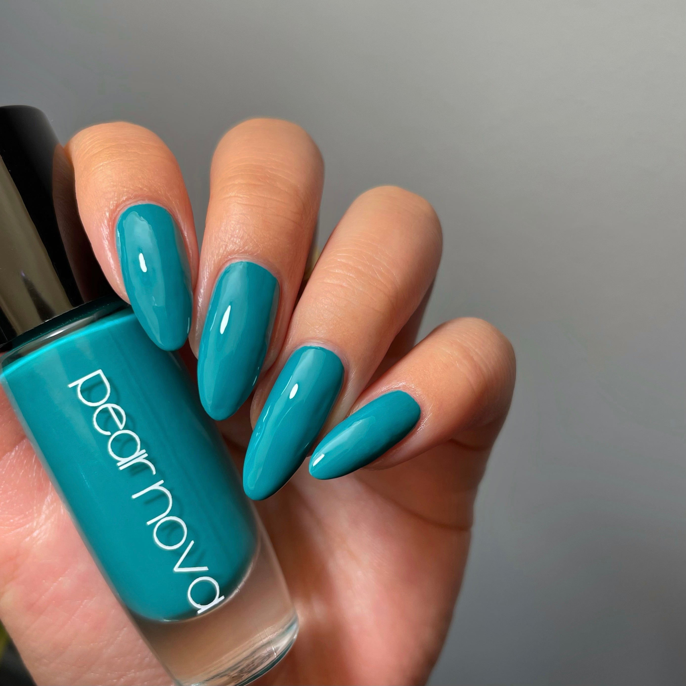 fair skin hand model holding bottle of nail polish with almond nails painted