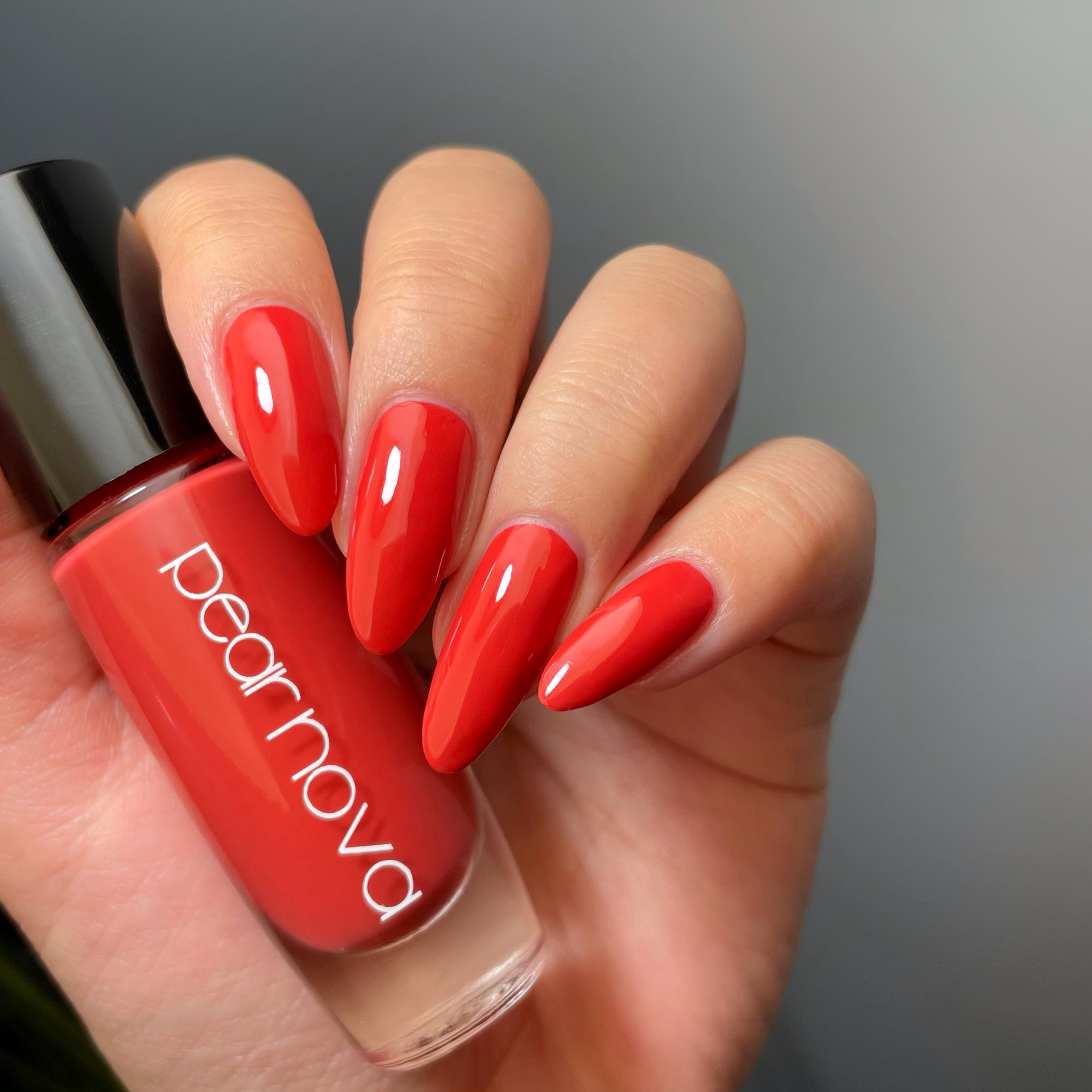 fair skin hand model holding bottle of nail polish with almond shaped nails painted