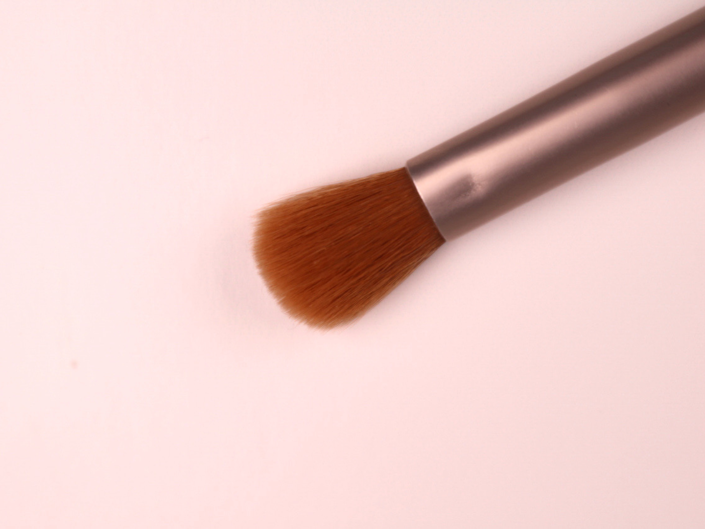 Makeup brush with brown bristles on a light pink background
