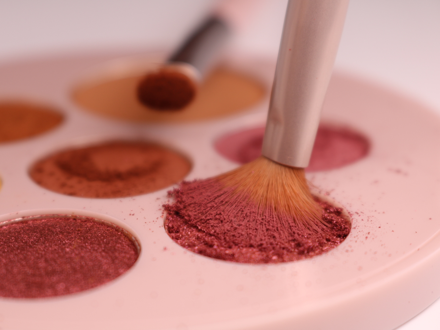 Makeup brush interacting with a pink makeup palette