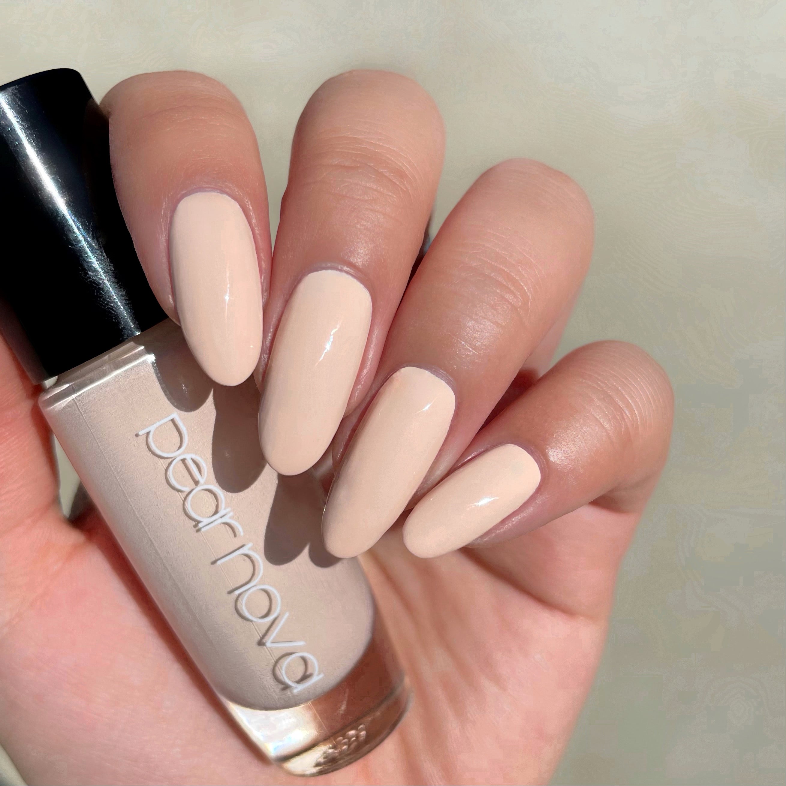 fair skin hand model holding bottle of nail polish with almond shaped nails painted beige